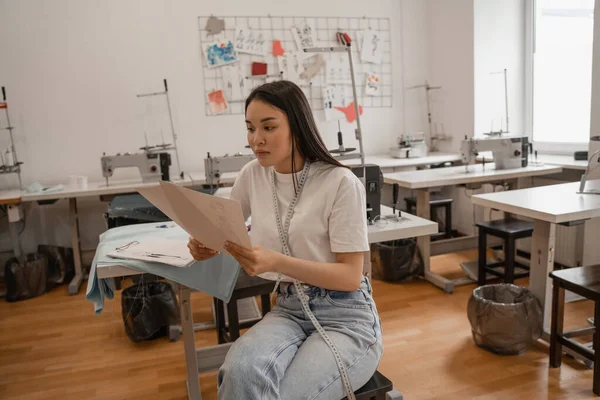 Diseñador asiático mirando bocetos en atelier - foto de stock