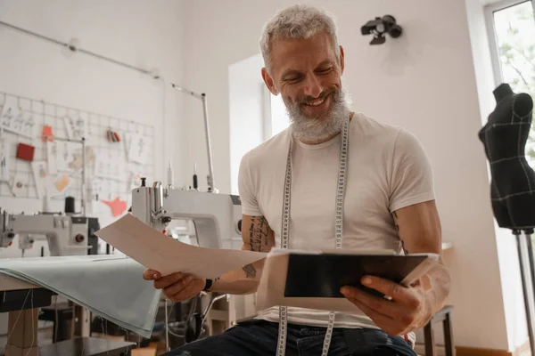 Cheerful designer holding papers and clipboard in atelier — Stock Photo