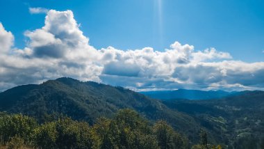 Bulutlu bir gökyüzünde yeşilliklerle kaplı güzel bir dağ görüntüsü.