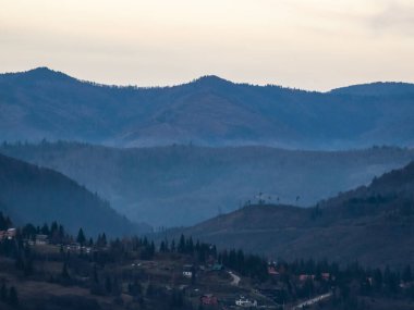 Sonbaharda dağ köyü üzerinde günbatımı ve ön planda ağaçlarla