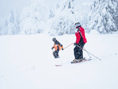 Baba ve kızı karlı dağlarda kayak yapıyor.