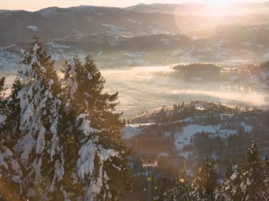 Karlı tepeler ve dağlardaki ağaçlarla kışın gün batımı.