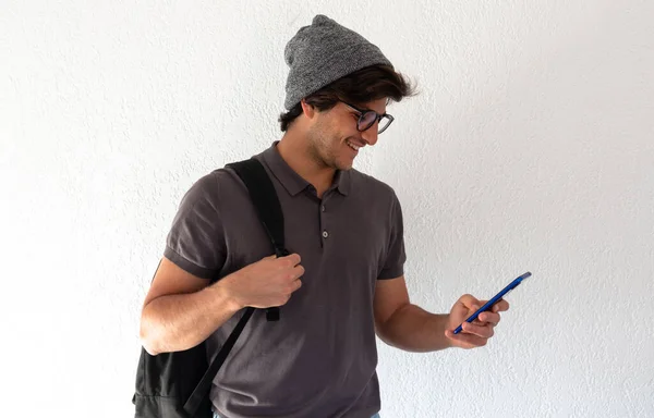 young man student standing carrying a backpack and chatting with a phone over white background