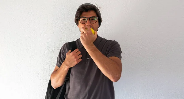 young man student standing eating an apple and carrying a backpack over white background