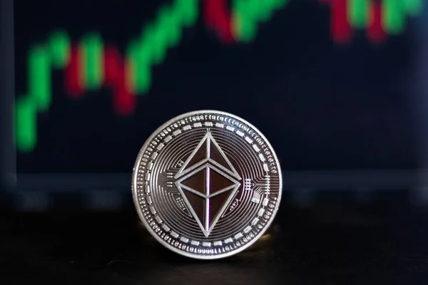 Ethereum 'un kripto gümüş sikkesi finansal ve ekonomik yatırımları temsil eden bir grafiğin önünde.