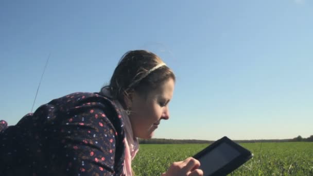 Mädchen mit Tablette im Gras liegend. Kamerafahrt mit dem Schieberegler — Stockvideo