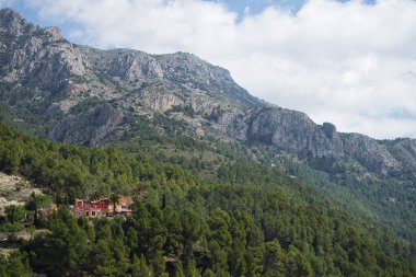 Ağaçlı güzel doğal manzara ve çam ormanlarının arasında kırmızı bir ev arka planda Guadalest, Alicante, İspanya 'da bulunan güzel bir dağın manzarası..