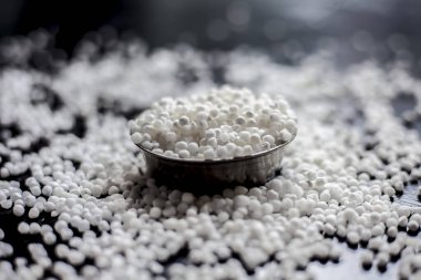 Siyah bir yüzey üzerinde cam bir tabakta çiğ sago incileri ya da tapyoka incileri yakın çekim.