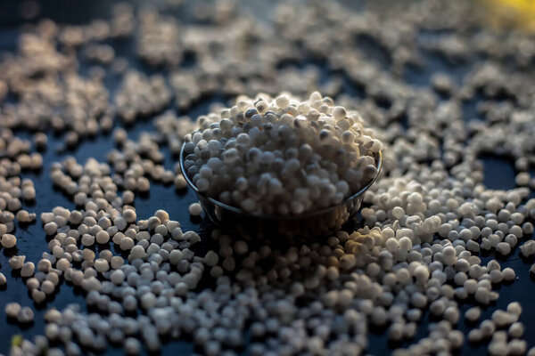Close up shot of raw sago pearls or tapioca pearls in a glass plate on a black colored surface.