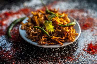 Bir cam tabakta Piyaz pakora / bhaji / bhajji / bhajji / bajji şat taze yeşil biber ve kırmızı biber tozu ile birlikte siyah yüzey.