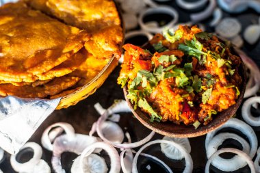 Batate ki sukhi bhaji ya da patates sabji 'yi kilden bir kaseyle yakın plan çek. Yanında da sade kızarmış puri ve siyah bir yüzeye kesilmiş soğan..