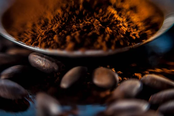 レンブラント照明と黒の色の木の板にいくつかの生のコーヒー豆とコーヒー粉のマクロショット — ストック写真