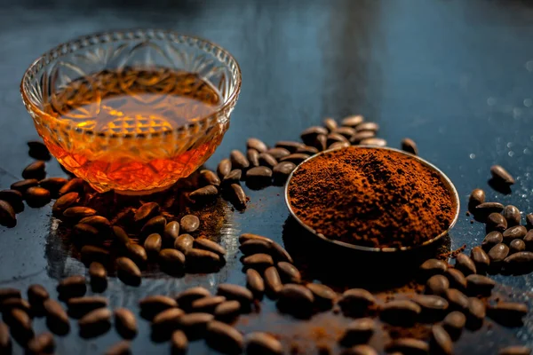 Coffee face mask for anti-aging on a black colored wooden surface consisting of some coffee beans and honey.