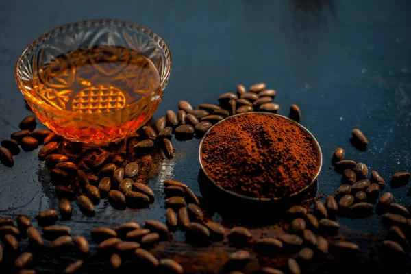 Coffee face mask for anti-aging on a black colored wooden surface consisting of some coffee beans and honey.