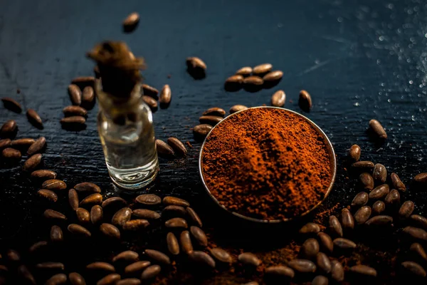 Coffee face mask for anti-aging on a black colored wooden surface consisting of some coffee beans and raw organic coconut oil in a small tiny glass bottle.