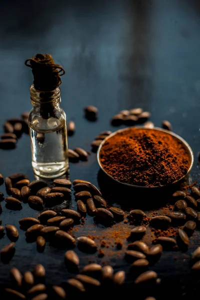 Coffee face mask for anti-aging on a black colored wooden surface consisting of some coffee beans and raw organic coconut oil in a small tiny glass bottle.