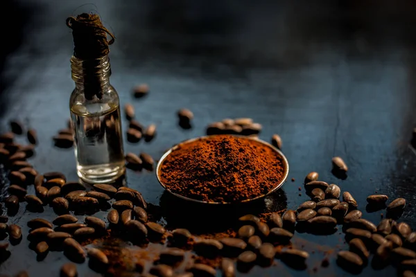 Coffee face mask for anti-aging on a black colored wooden surface consisting of some coffee beans and raw organic coconut oil in a small tiny glass bottle.