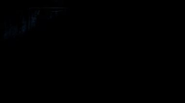 Dramatik ışıklandırmada uzun siyah bir ceket giyen bir adamın alt kata taşınması..