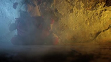 Duvarın yanında oturan oyuncak ayının dramatik ışıklandırmayla etrafı dumanla çevrili ve çerçevede bir yabancının çizmeleriyle çekilmiş fotoğrafı..