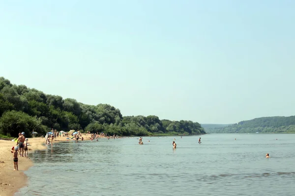 Nice view of the river. People are swimming. Beach. In a rural area. Around nature.