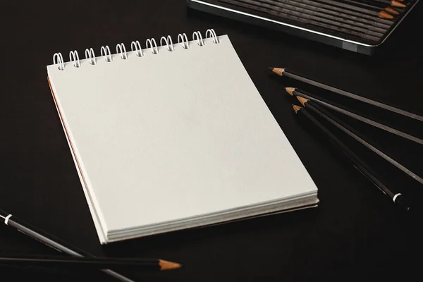 Blank notepad with white sheets on a dark table background. Top view writing mockup great for adding any drawing. Glasses and pencils in a background. Small focal length.