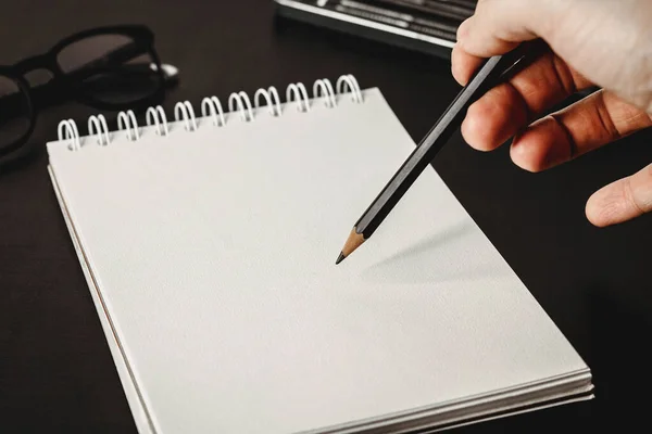 Blank notepad with white sheets on a dark table background. Drawing hand mockup great for adding any image. Small focal length. Glasses and pencils in a background.