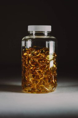 İlaç renkli haplar kavanozda, kapsüller koyu renkli arka planda dikey teçhizatla işaretlenmiş. Tıbbın yaratıcı kavramları. 