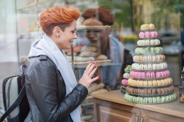 Mulher olha para vitrine com bolos coloridos — Fotografia de Stock