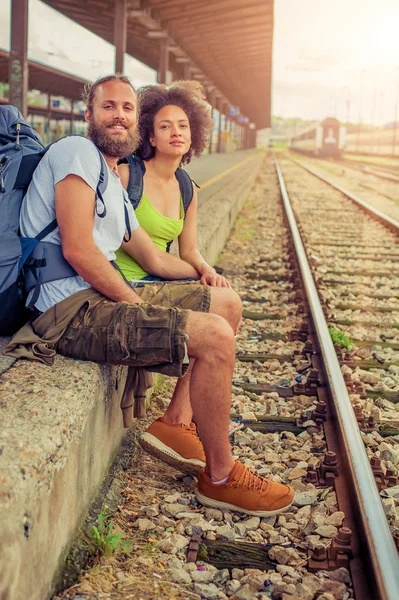 Счастливая молодая и красивая пара туристов, сидящих у железной дороги — стоковое фото