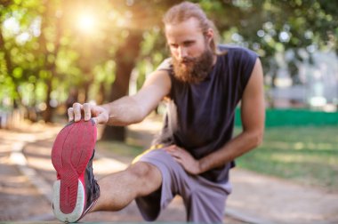 Açık havada eğitim. Genç adam bacaklarını esnetiyor.