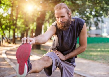 Açık havada eğitim. Genç adam bacaklarını esnetiyor.