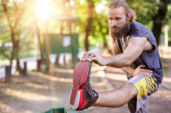 Açık havada eğitim. Genç adam bacaklarını esnetiyor.