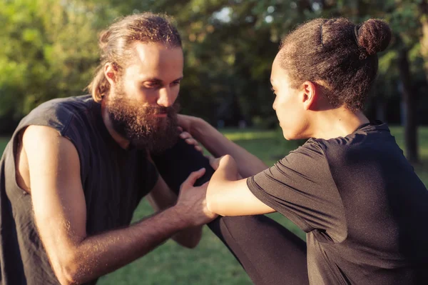 Entrenamiento al aire libre. Pareja joven estirando las piernas entre sí . — Foto de Stock