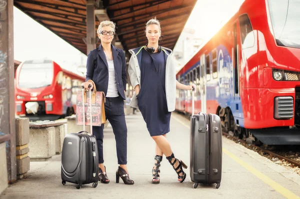 Две элегантные женщины с чемоданом позируют на железнодорожном вокзале — стоковое фото