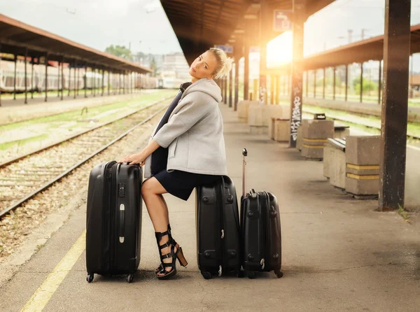Элегантная женщина сидит на чемоданах и ждет поезда — стоковое фото