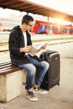 Gazete okuyan demiryolu platformu üzerinde oturan adam