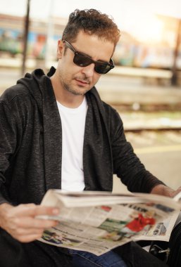 Gazete okuyan demiryolu platformu üzerinde oturan adam