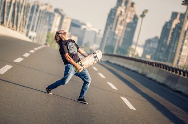 Happy skateboarder on the bridge playing guitar on his skate 