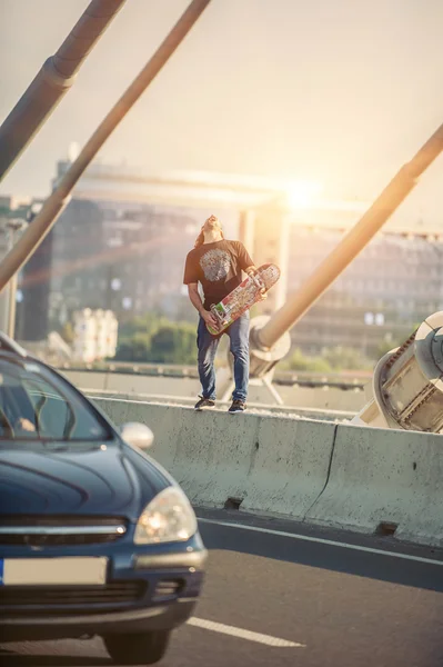 Happy skateboarder on the bridge playing guitar on his skate — Stock Photo, Image