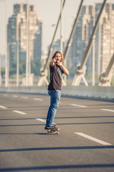 Skateboardista stojí na mostě a ukazoval na vás — Stock fotografie