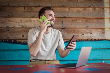 Genç çılgın hippi cep telefonuyla konuşuyor, tablet kullanıyor ve dizüstü bilgisayara bakıyor. İnternet bağlantısı, ağ kurma. Aygıt elektroniği aygıtı kavramı