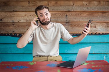 Genç çılgın hippi cep telefonuyla konuşuyor, tablet kullanıyor ve dizüstü bilgisayara bakıyor. İnternet bağlantısı, ağ kurma. Aygıt elektroniği aygıtı kavramı
