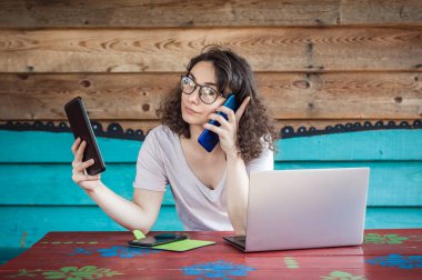 Genç çılgın hippi cep telefonuyla konuşuyor, tablet kullanıyor ve dizüstü bilgisayara bakıyor. İnternet bağlantısı, ağ kurma. Aygıt elektroniği aygıtı kavramı