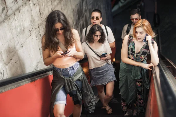 友人のグループは エスカレーターの上に立っている間 スマートフォンで話します 携帯電話の屋外の近代的な人々 モバイル通信技術 高角度表示 — ストック写真