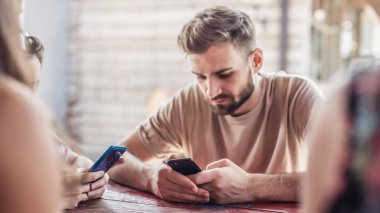 Yabancılaşma bağımlılığı. Bir grup arkadaş kafede oturup kendi telefonlarıyla yazıyorlar.