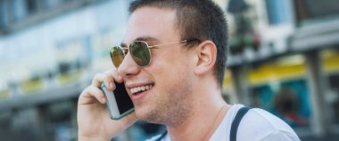 Şehir merkezinde yürüyen ve konuşan mutlu genç adam. Gençler yeni teknoloji eğilimlerine bağımlı. Gençlik, yeni nesil internet arkadaşlık kavramı