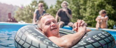 Yüzme havuzunda yüzen mutlu genç adam şişme yüzüklerle ve arkadaşlarıyla yazın tadını çıkarıyor.