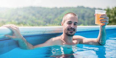 Mutlu genç adam bira içer ve havuzda eğlenir.