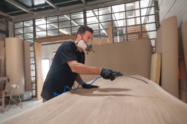 Solunum maskeli bir adam atölyedeki tahtaları boyuyor. Sanatçı modern mobilya fabrikası boyası