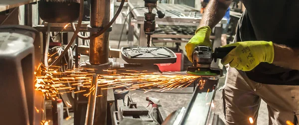 在工厂的钢结构上用电动磨床工具工作的人 闪烁着火花 操作中的磨床 — 图库照片